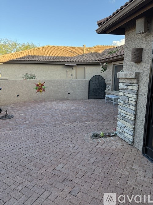 A brick patio leads to a house with a black gate.