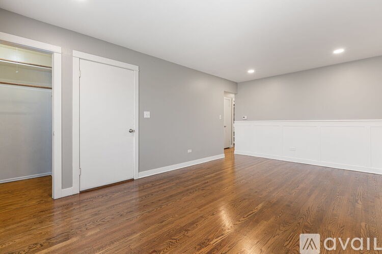 A room with wooden floors and white walls, with a door on the left and a window on the right.