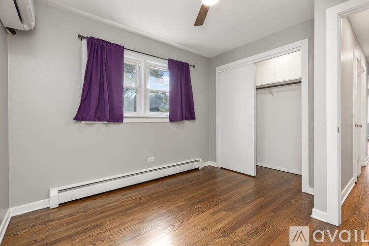 A room with a window covered by purple curtains and wooden flooring.