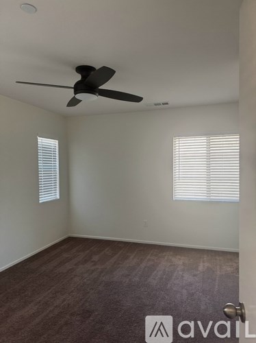 A room with a ceiling fan and two windows.