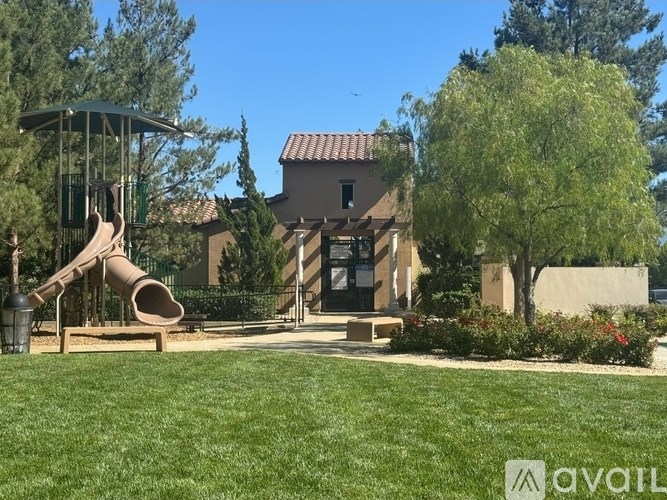 A playground with a slide and a tree in front of a house.