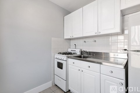 A white kitchen with a stove, sink, and cabinets.