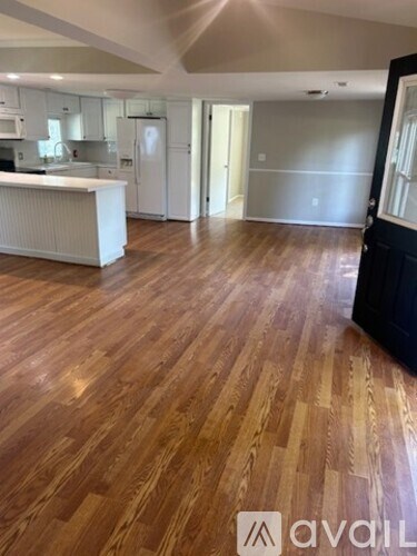 A spacious room with wooden flooring and a kitchen area.