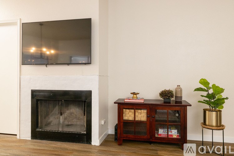 A black fireplace with a wooden cabinet above it and a plant on a stand to the right.