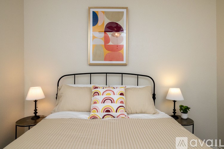 A bed with a striped comforter and two striped pillows with a painting on the wall above it.
