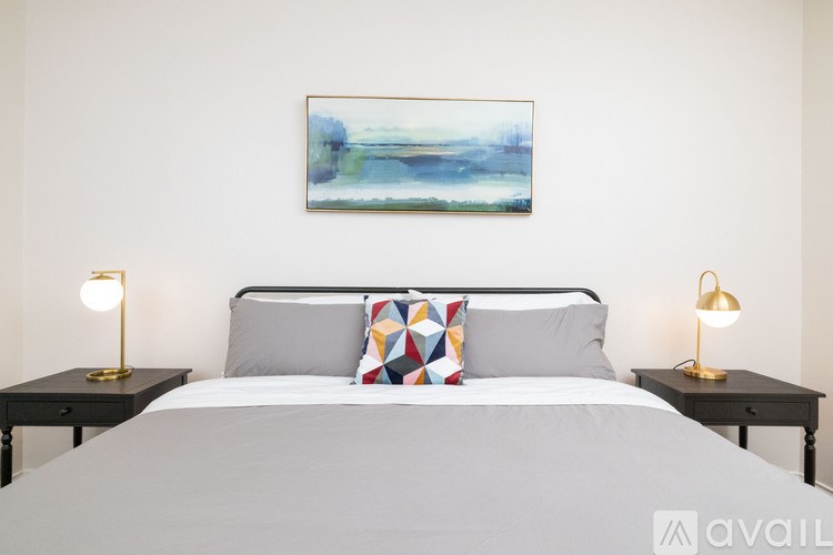 A bedroom with a large bed, two lamps, and a painting on the wall.