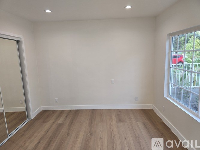 A room with wooden flooring and a window overlooking a red vehicle.