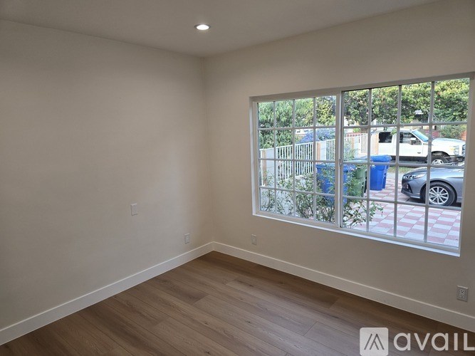 A room with a large window overlooking a street with cars and a trash can.