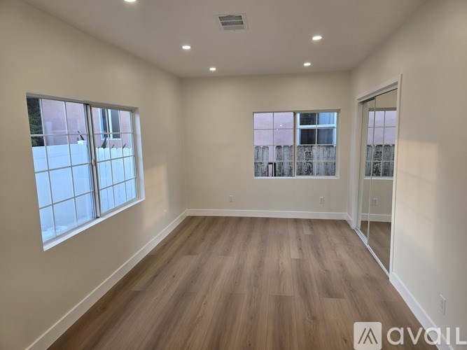 A spacious room with wooden flooring and large windows.