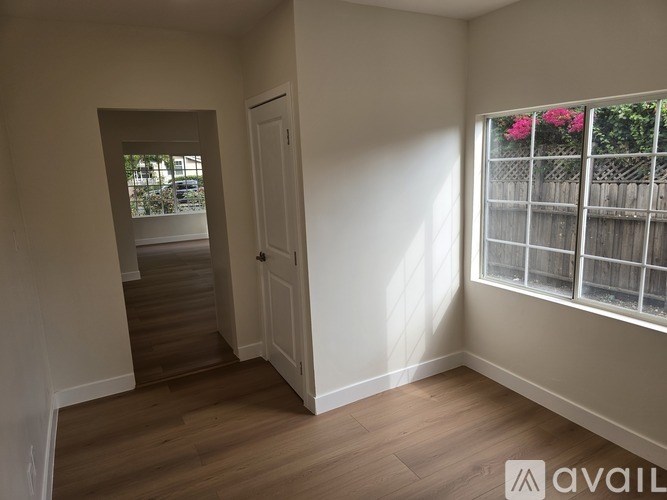 A room with a door and a window with a view of a fence and flowers.