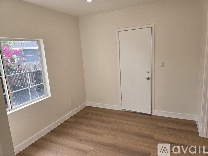 A room with a white door and a window with a view of a fence and flowers outside.
