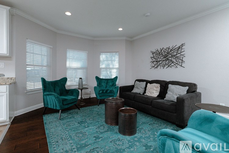 A living room with a black couch, two green chairs, and a blue rug.