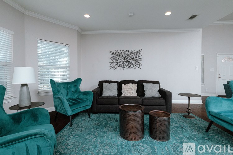 A living room with a black couch, two green chairs, and a large abstract art piece on the wall.