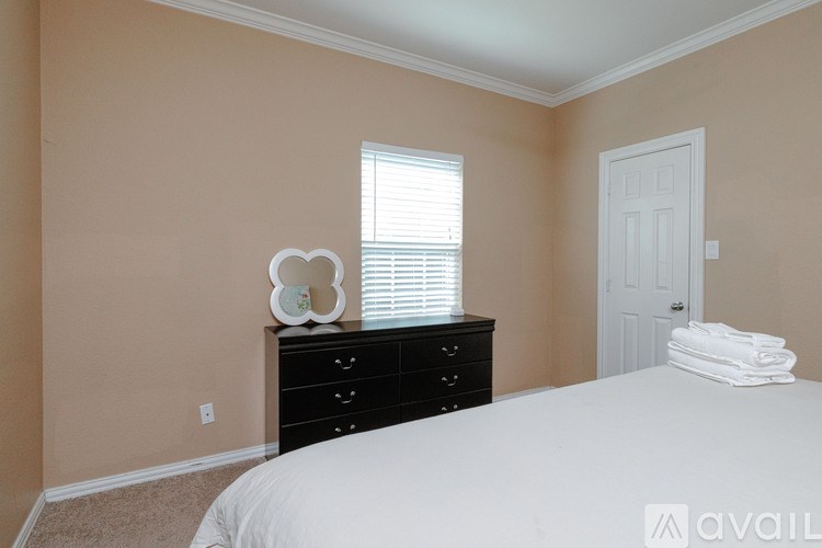A bedroom with a white bed, a black dresser, and a white door.
