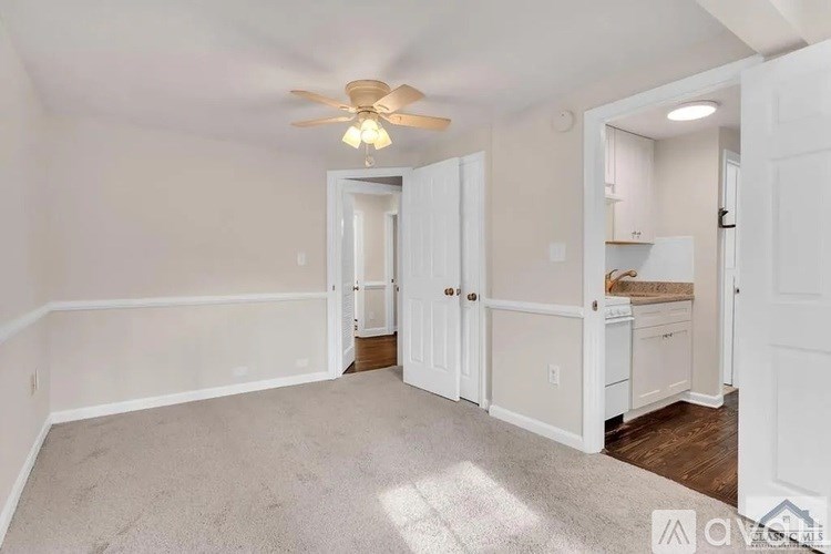 A spacious room with a ceiling fan and light, carpeted floor, and white walls.