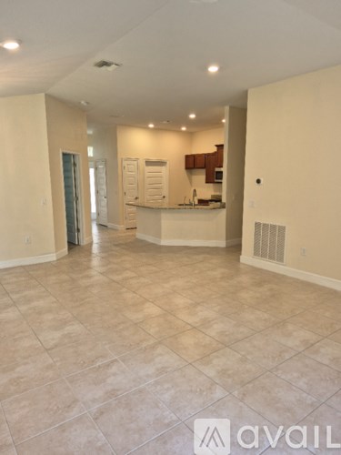 A spacious room with tiled flooring and a kitchen area in the background.