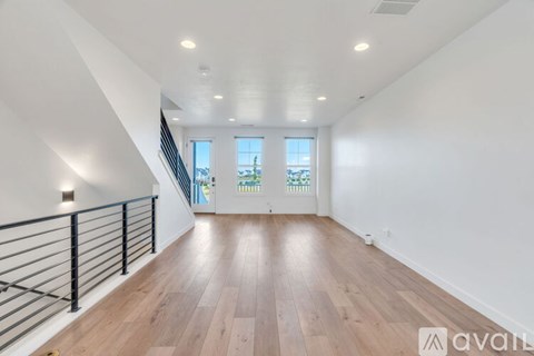 A spacious room with wooden floors and a staircase with a metal railing.