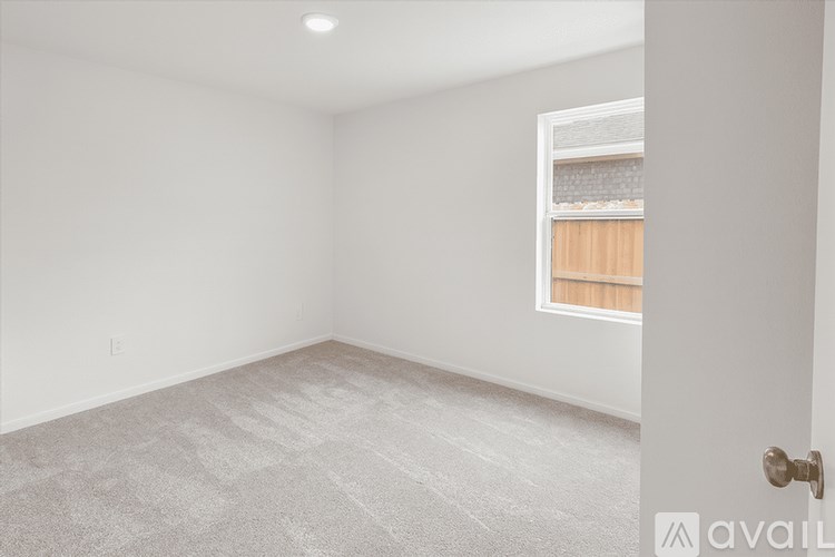 A room with a carpeted floor and a window with a view of a wooden fence.
