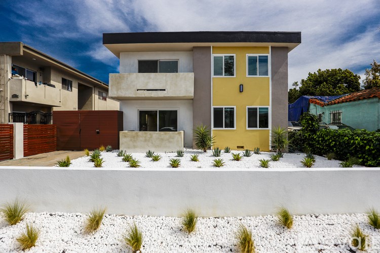 A modern house with a yellow and white facade stands in front of other buildings.