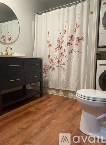 A white toilet sits in a bathroom with a shower curtain featuring pink flowers.