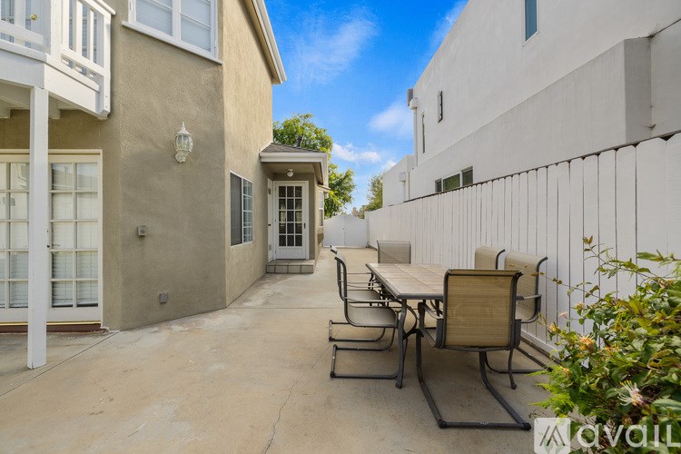 A patio with a table and chairs is surrounded by a white wall and a tan building.