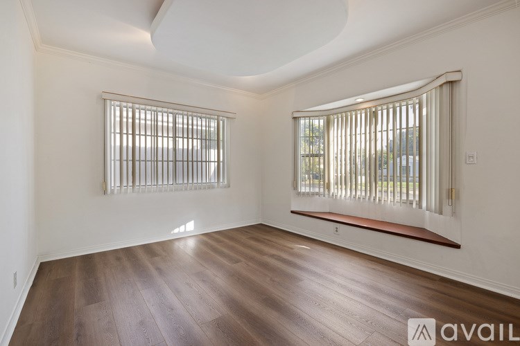 A room with wooden floors and two windows with blinds.