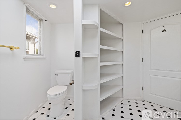 A white bathroom with a toilet and a shelving unit.