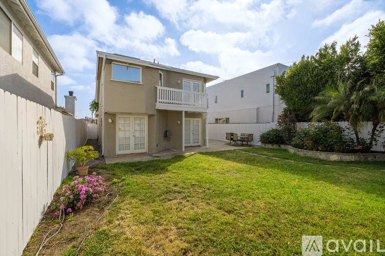 A sunny day at a two-story house with a balcony and a garden.