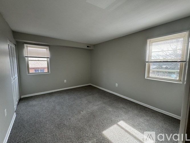 A room with a carpeted floor, a window with blinds, and a door on the left side.