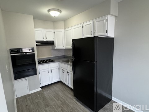 A black refrigerator stands in a kitchen with white cabinets.