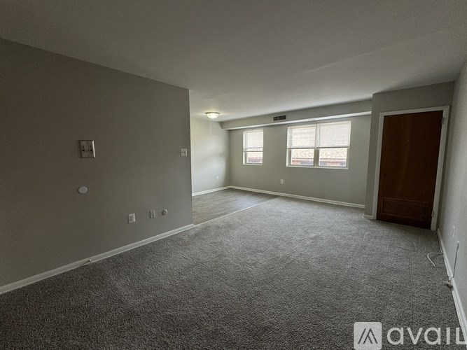 A spacious room with grey carpeting and a brown door.