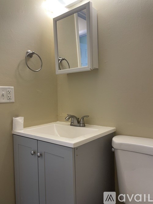 A bathroom with a white sink and grey cabinet.