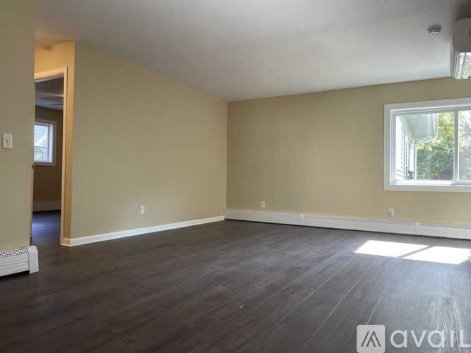 A spacious room with wooden floors and a window letting in natural light.