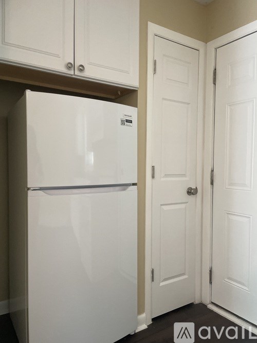 A white refrigerator in a kitchen with white cabinets.