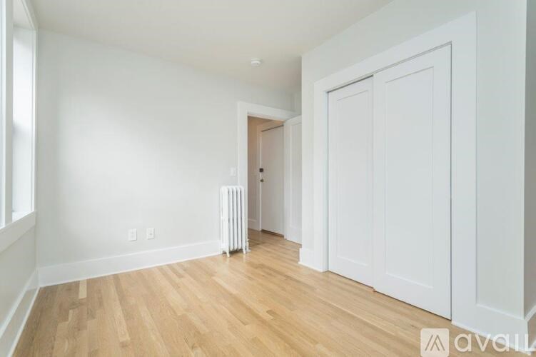 A room with white walls and wooden flooring, featuring a white radiator and a white door.