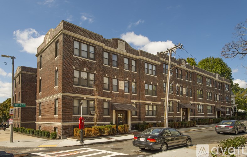A street view of a red brick building with cars parked in front.