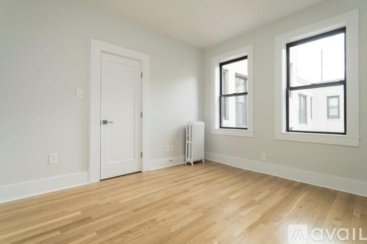 A room with a white door, a window, and a radiator on the floor.