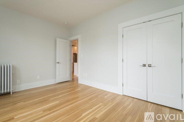 A room with white walls and wooden flooring, featuring a white door and a white cabinet.
