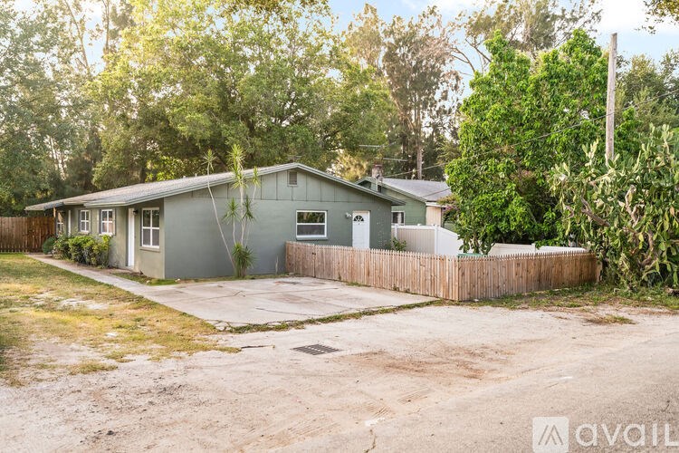A house with a grey exterior is surrounded by a wooden fence and greenery.