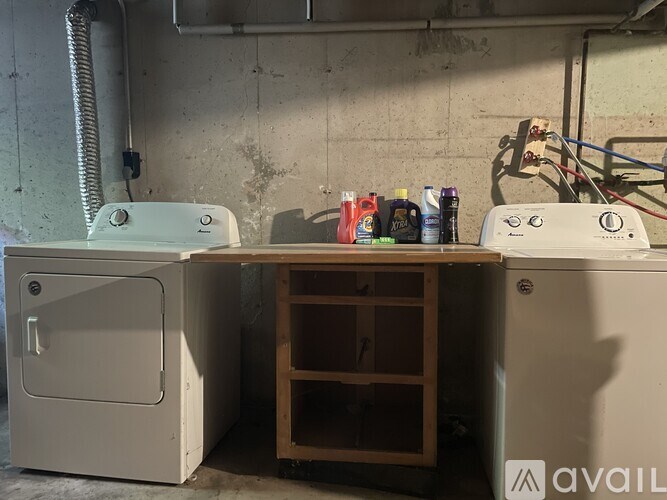 A white washing machine is in front of a concrete wall with a wooden shelf underneath it.