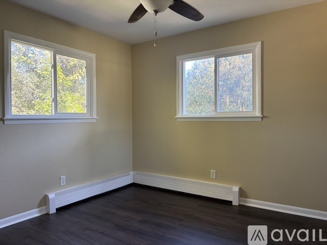 A room with a ceiling fan and two windows.