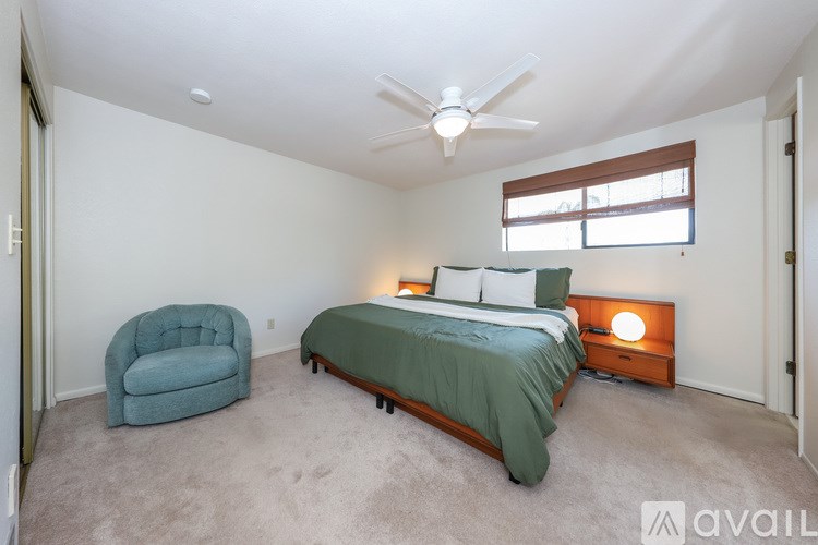 A bedroom with a bed, chair, and ceiling fan.