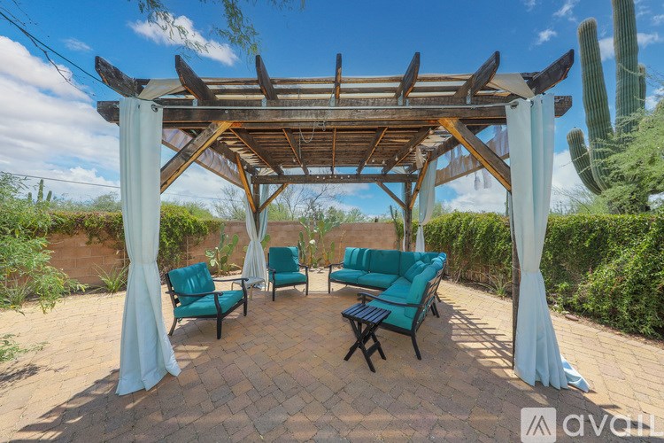 A wooden pergola with white curtains and a brick patio with green chairs.