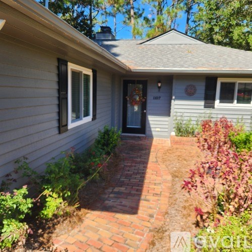 A house with a grey siding and a black door is surrounded by greenery.