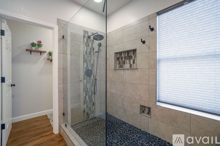 A bathroom with a walk-in shower and a window with blinds.