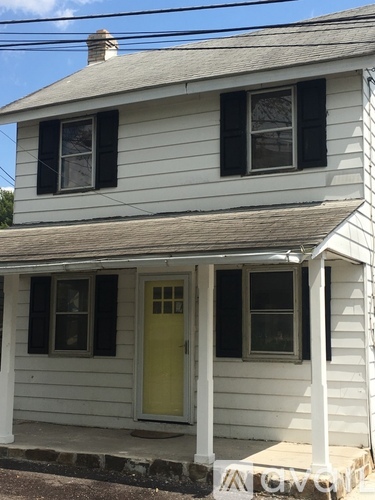 A small white house with a yellow door and a porch.