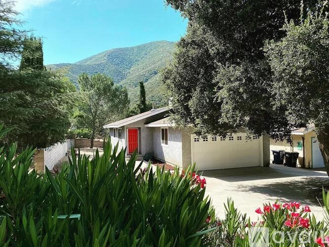A house with a red door is surrounded by greenery and flowers.