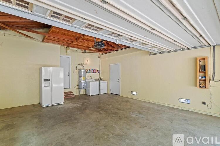 A large empty room with a kitchenette and a refrigerator.