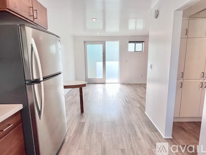 A kitchen with a refrigerator, wooden floors, and a bench.