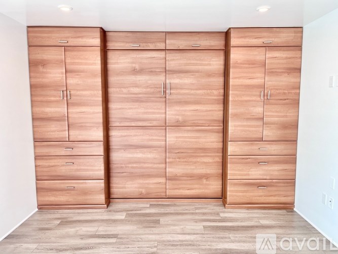 Three wooden wardrobes with drawers are in a white room.